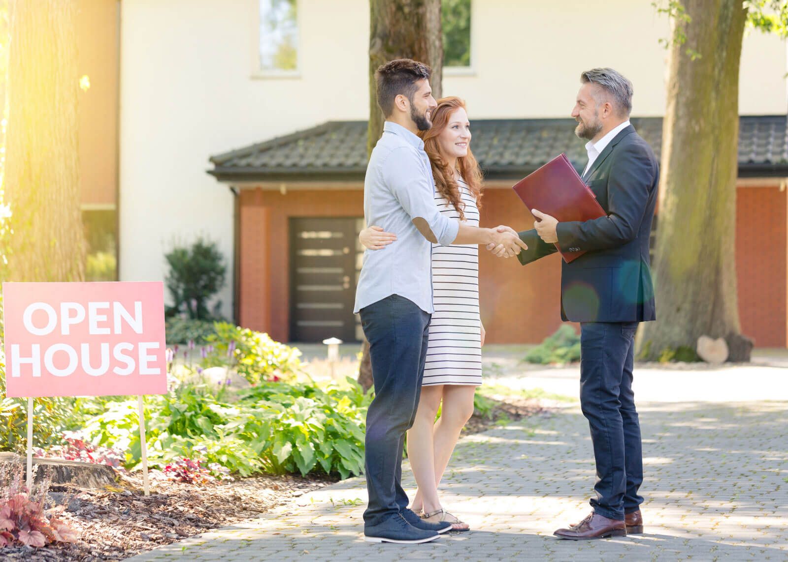 A man and woman are shaking hands with a real estate agent in front of an open house.