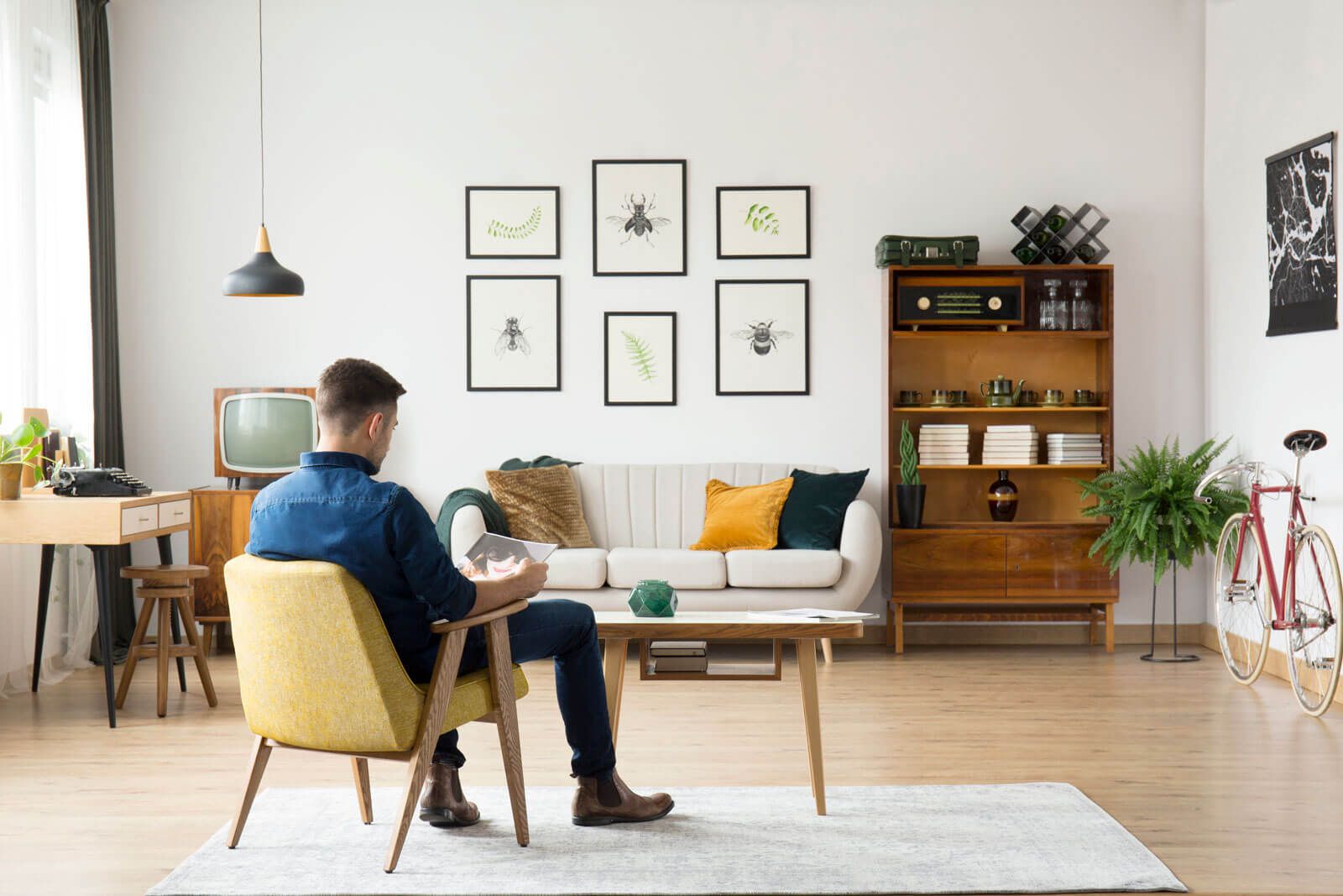 A man is sitting in a chair in a living room reading a book.