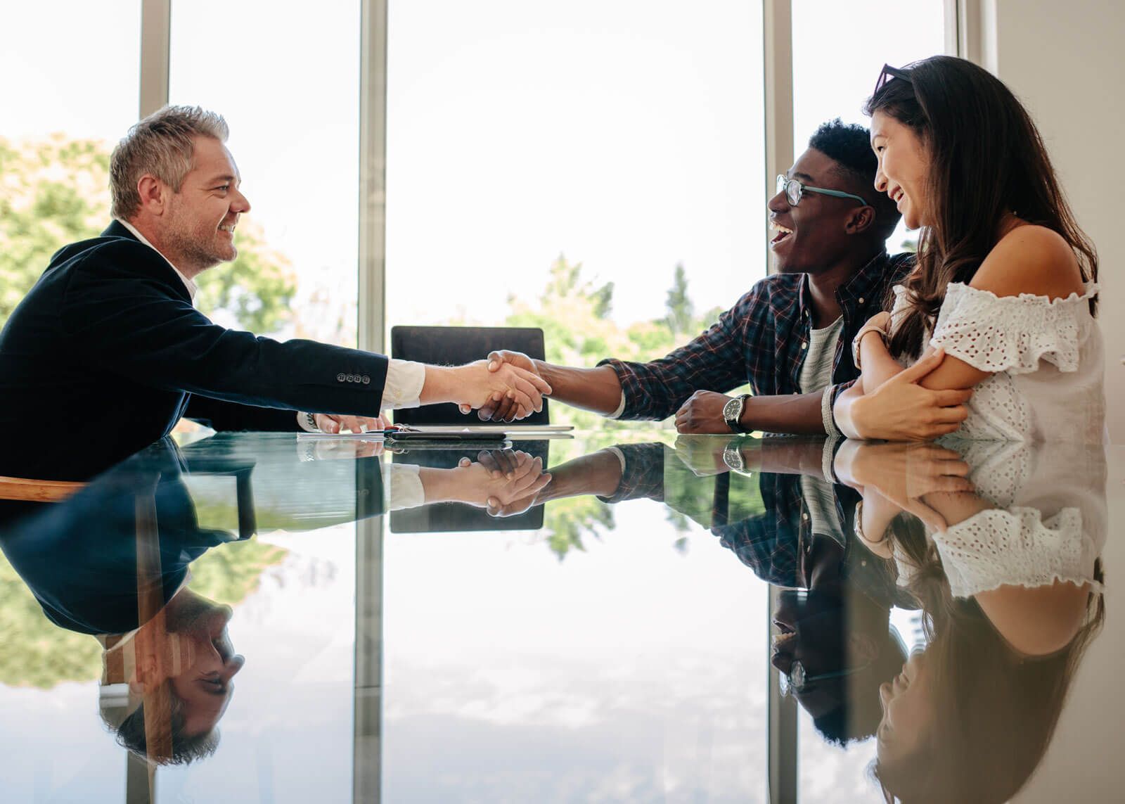 A man and woman are shaking hands while sitting at a table.