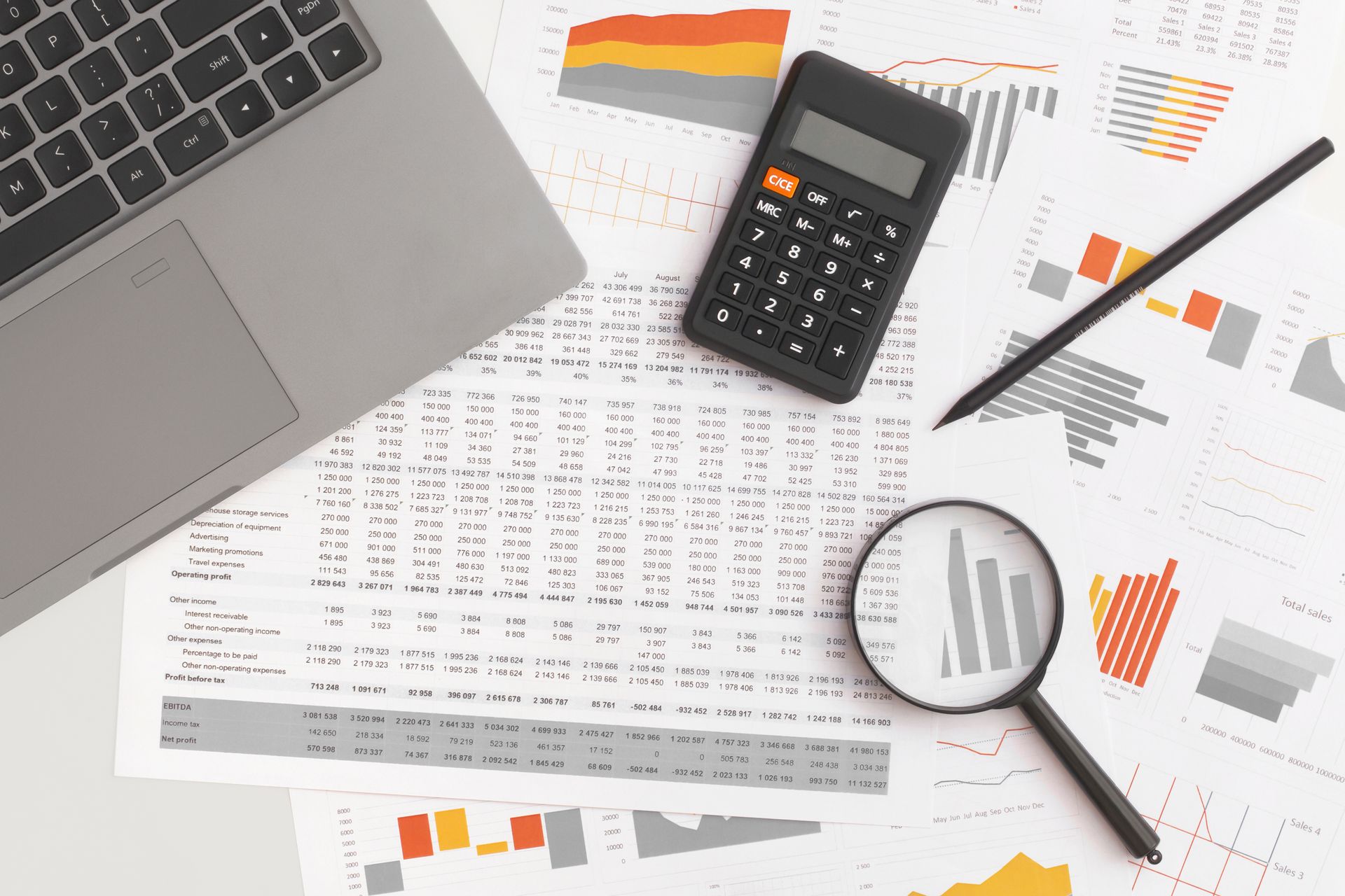 A magnifying glass is sitting on top of a table next to a laptop and a calculator.