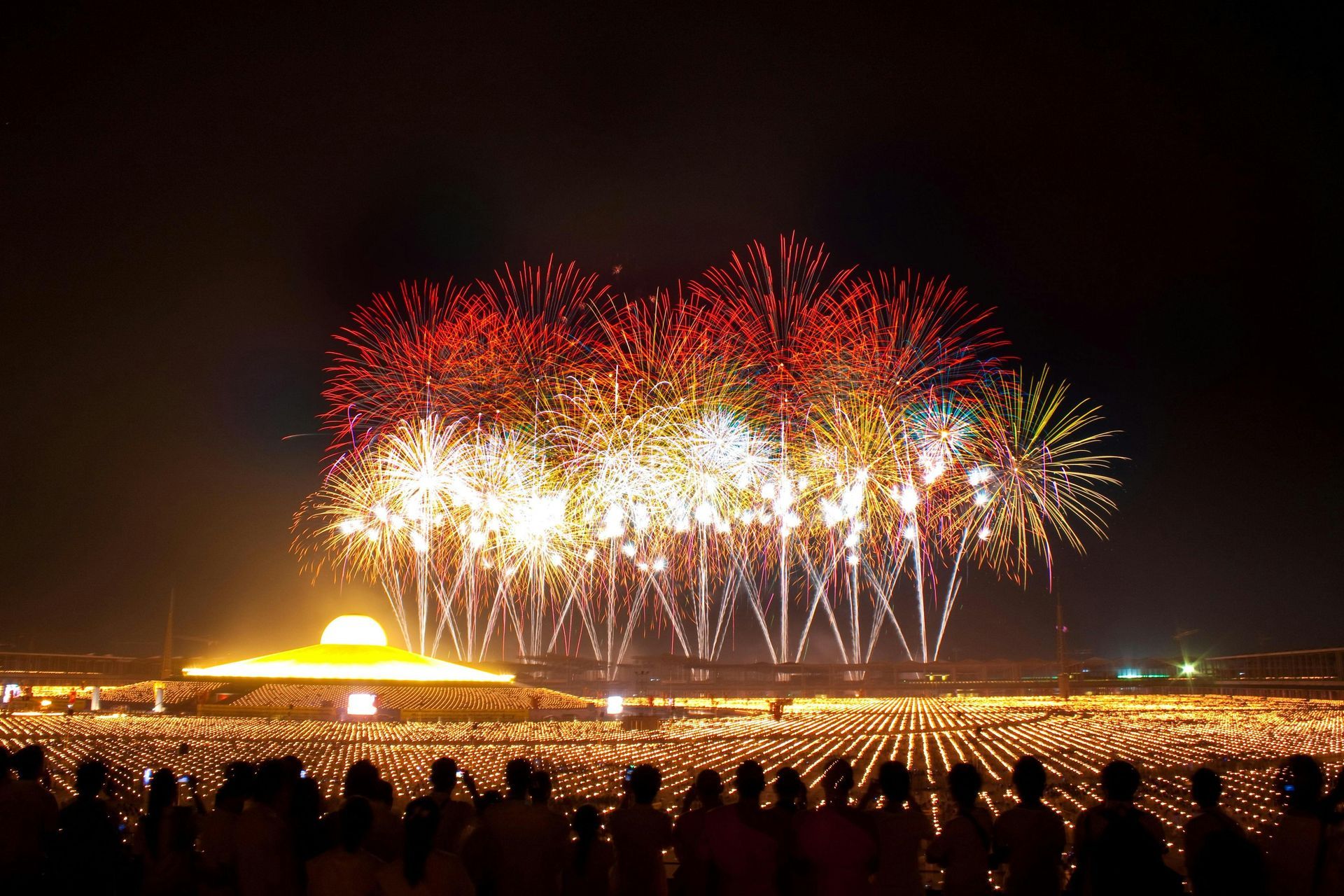 A large fireworks display is being watched by a crowd of people.