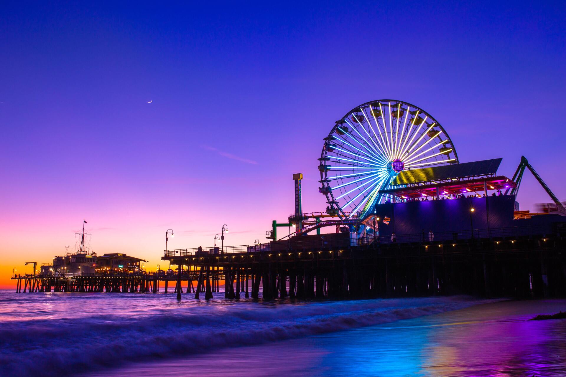 A pier with a ferris wheel in the background at sunset.