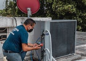 Technician inspecting rooftop HVAC unit with tools beside a red satellite dish