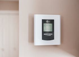 Wall-mounted digital thermostat with white frame on a beige wall