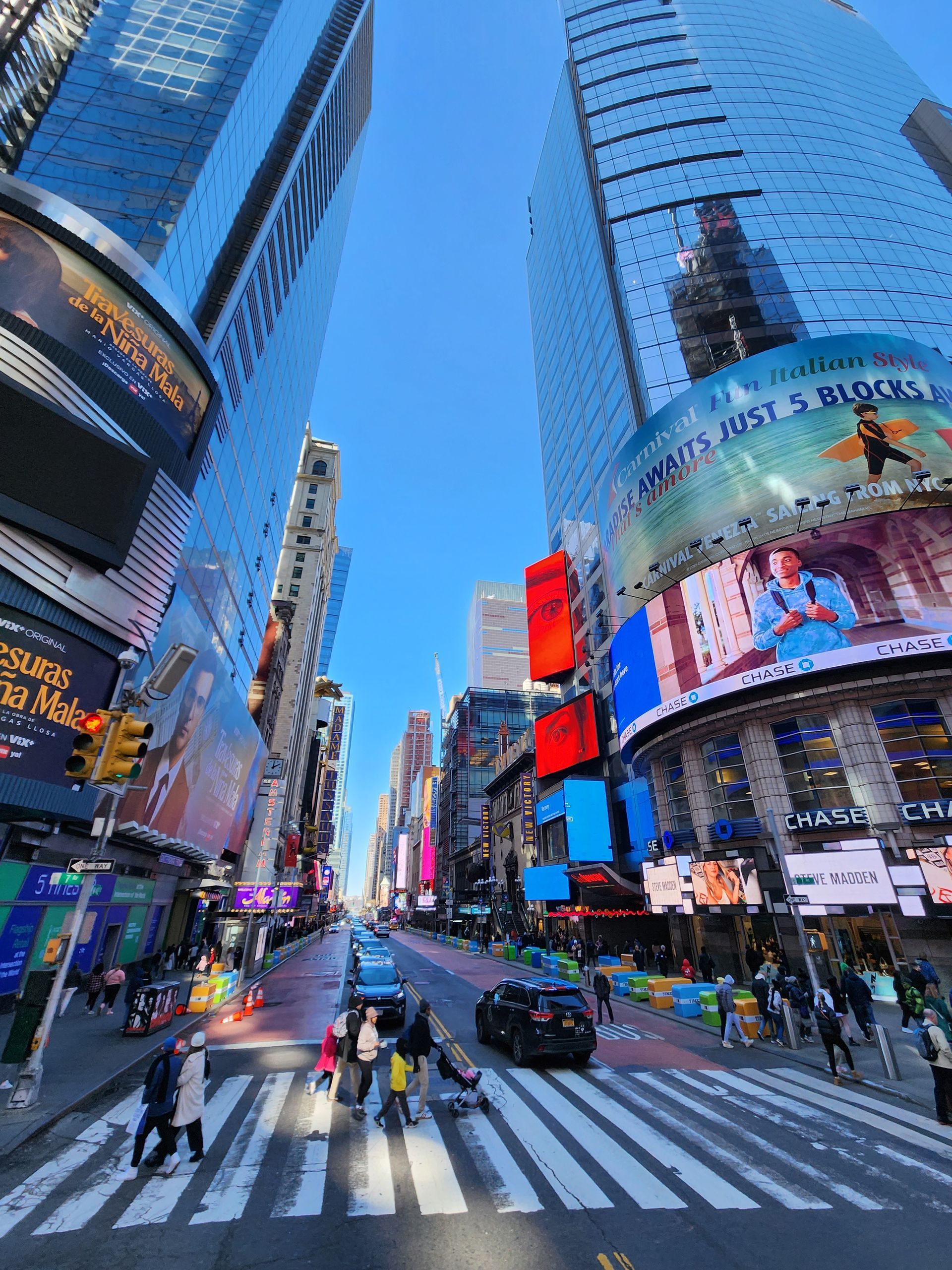 Busy Times Square intersection with tall digital billboards and pedestrians crossing a zebra crosswalk