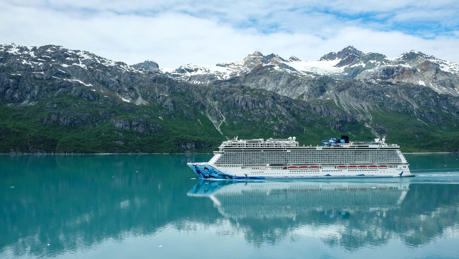 Cruise ship on turquoise water with snowcapped mountains reflected in the calm fjord