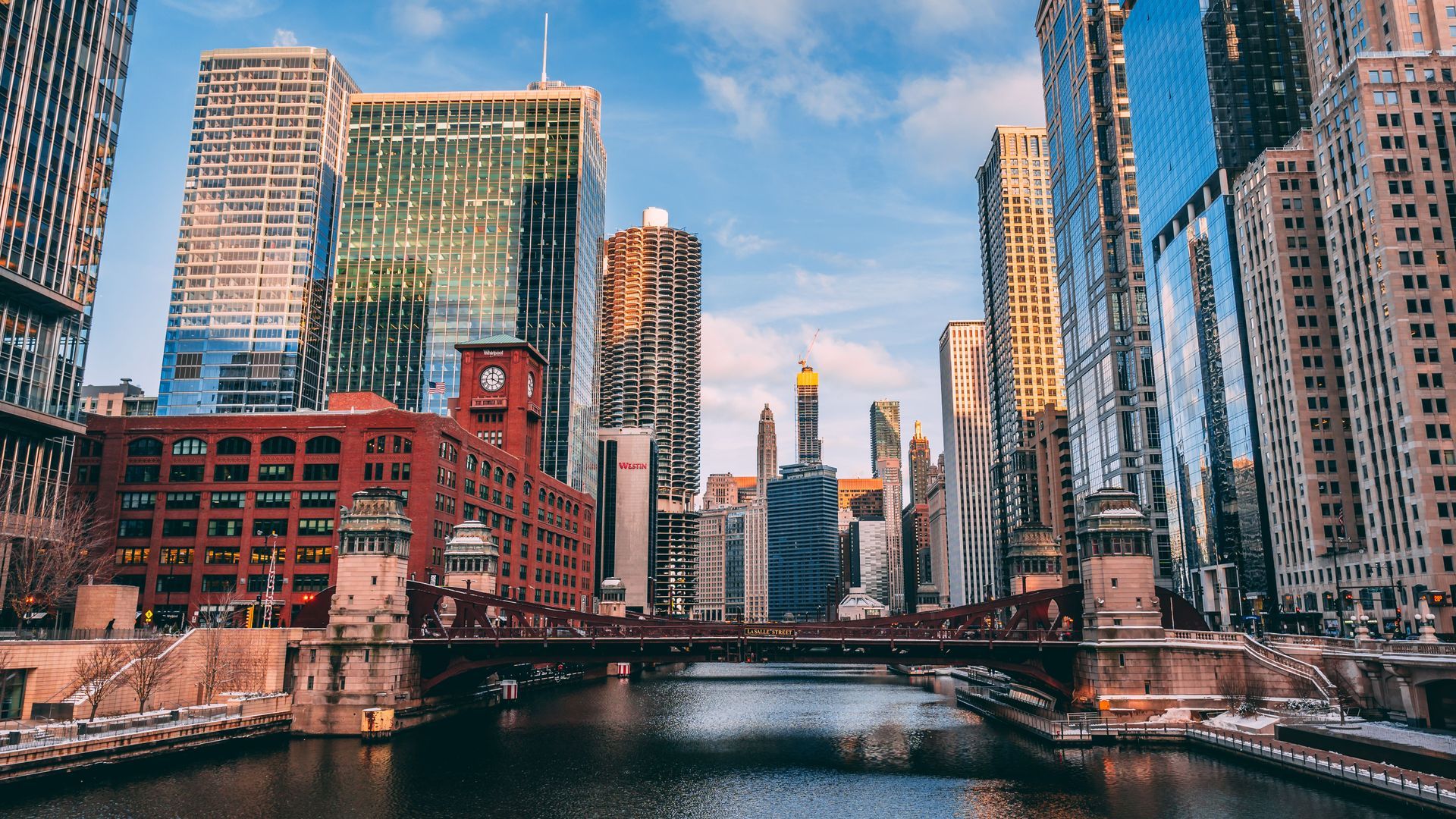 Downtown cityscape with tall glass skyscrapers and a bridge over a river at sunset