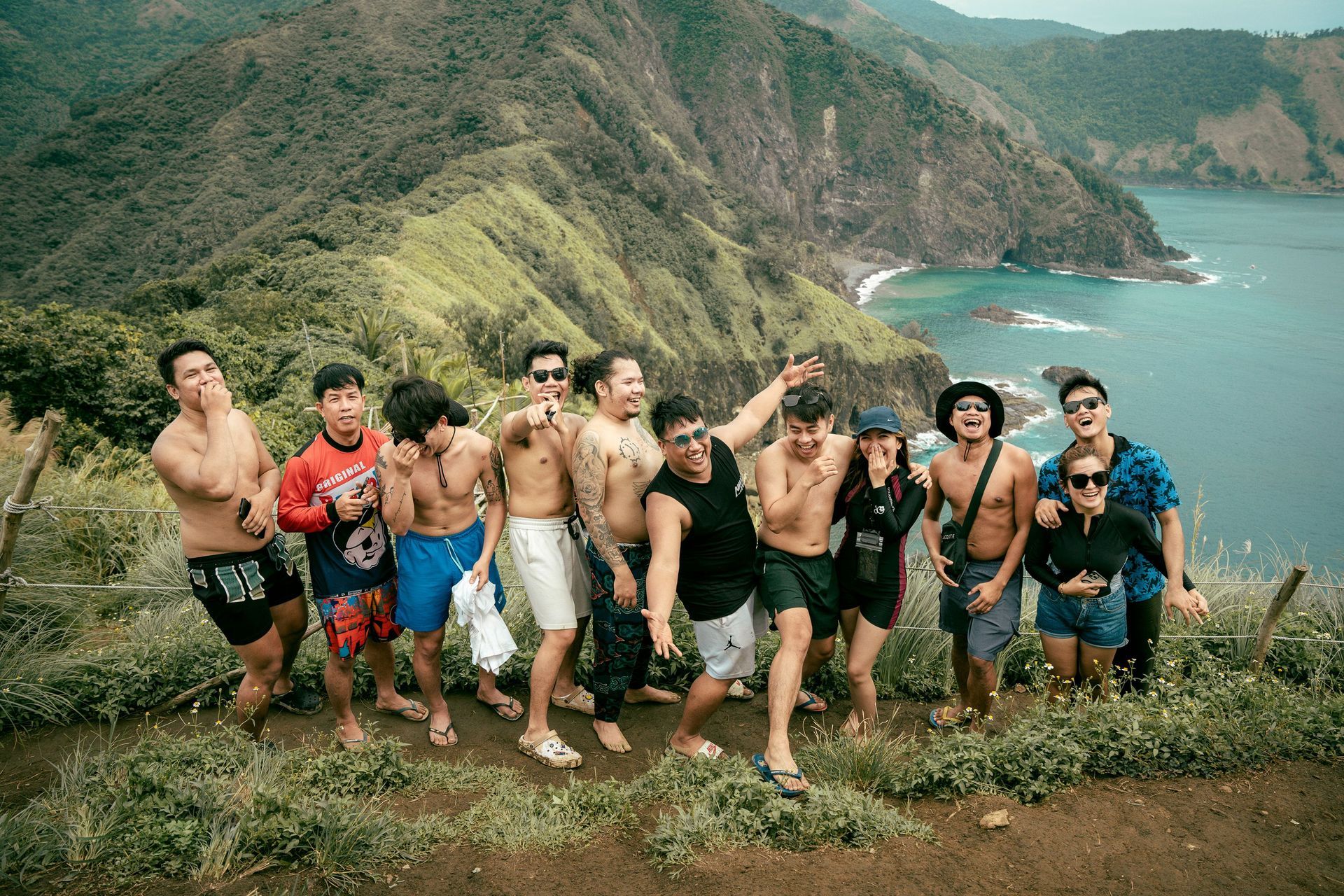 Group of people posing on a cliff with ocean and green mountains in the background.