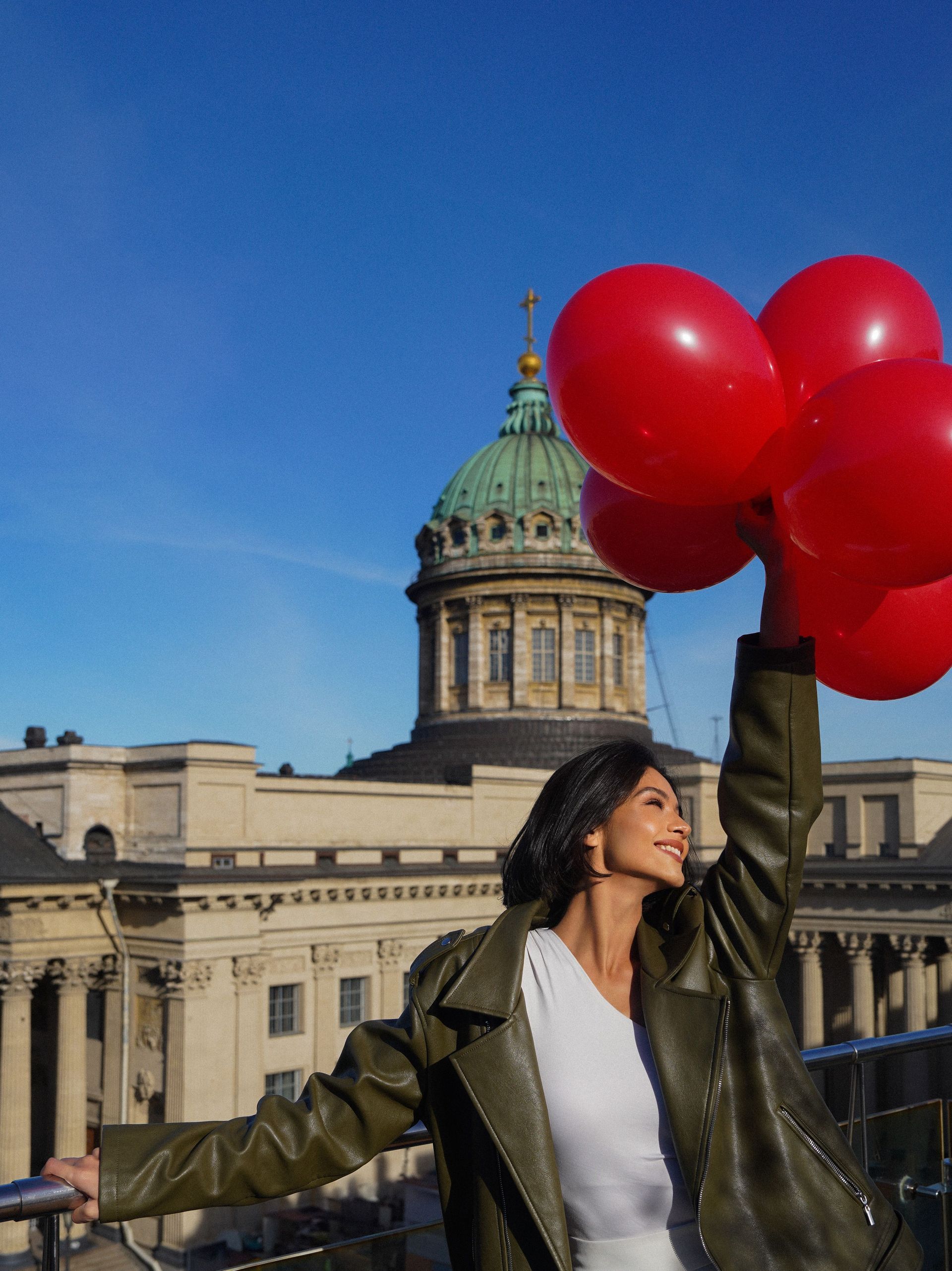 Woman holding red balloons in front of a domed historic building under a blue sky