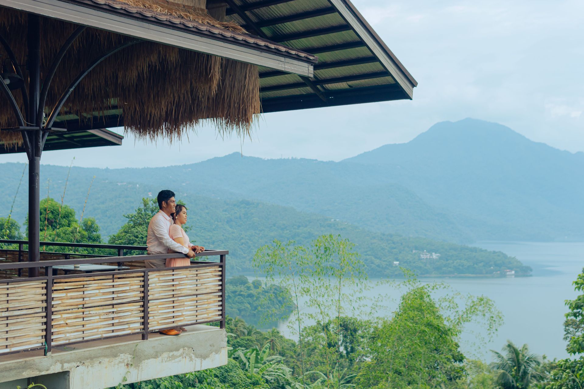 Person sitting on a balcony overlooking a lake and mountains under a cloudy sky