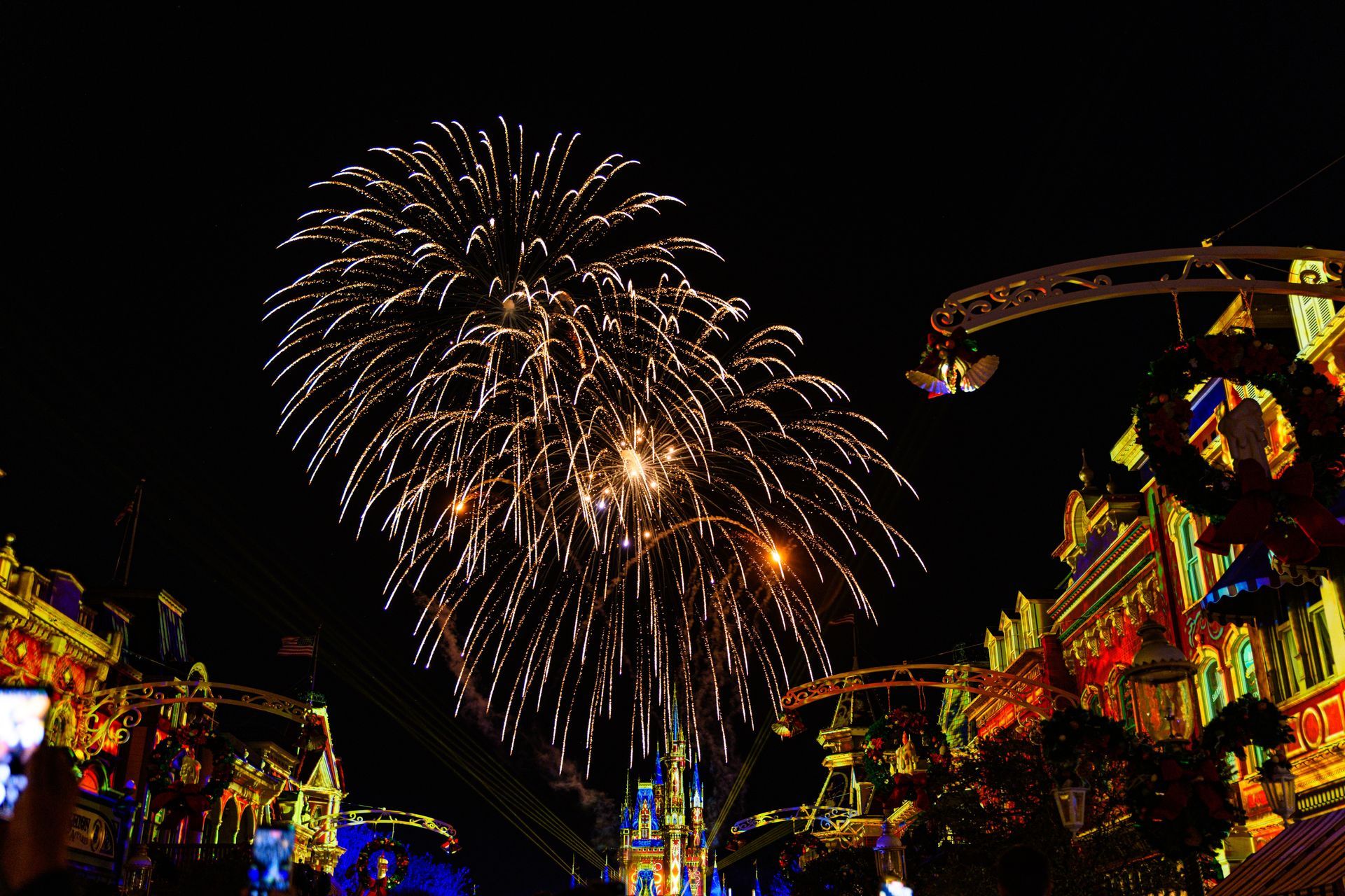 Fireworks bursting over a brightly lit street at night with colorful festival decorations