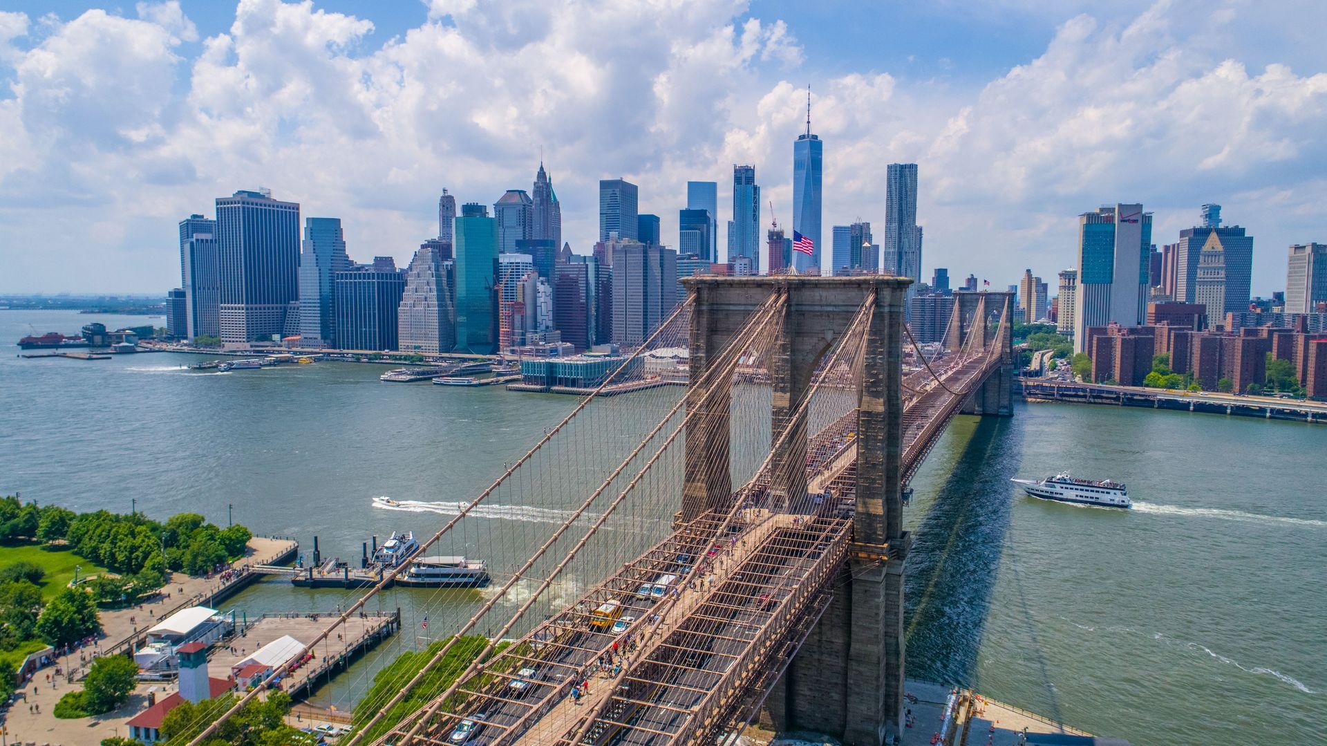Brooklyn Bridge leading to Manhattan skyline over the East River under a bright cloudy sky