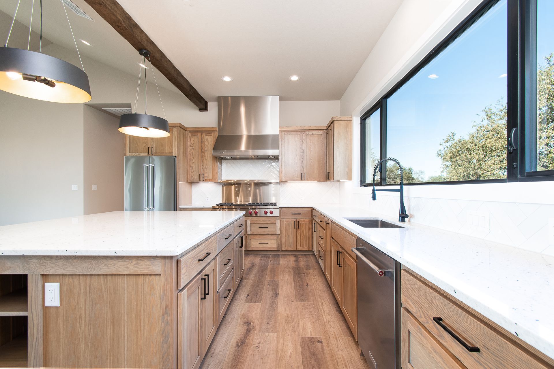 Bright modern kitchen with wood cabinets, white counters, island, and large window overlooking trees