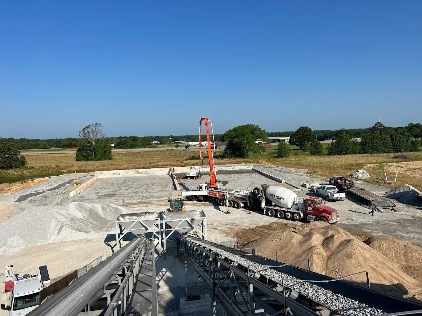 Construction site with concrete mixer truck and boom pump over a large excavation under a clear blue sky