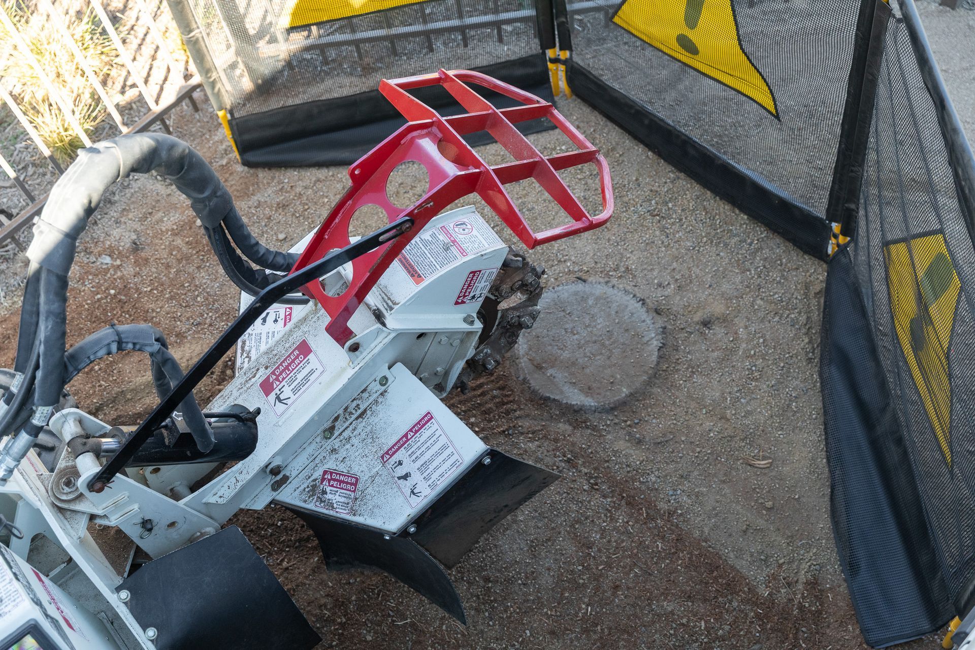 Red-and-white chainsaw lying on gravel beside black mesh fencing and yellow caution tape