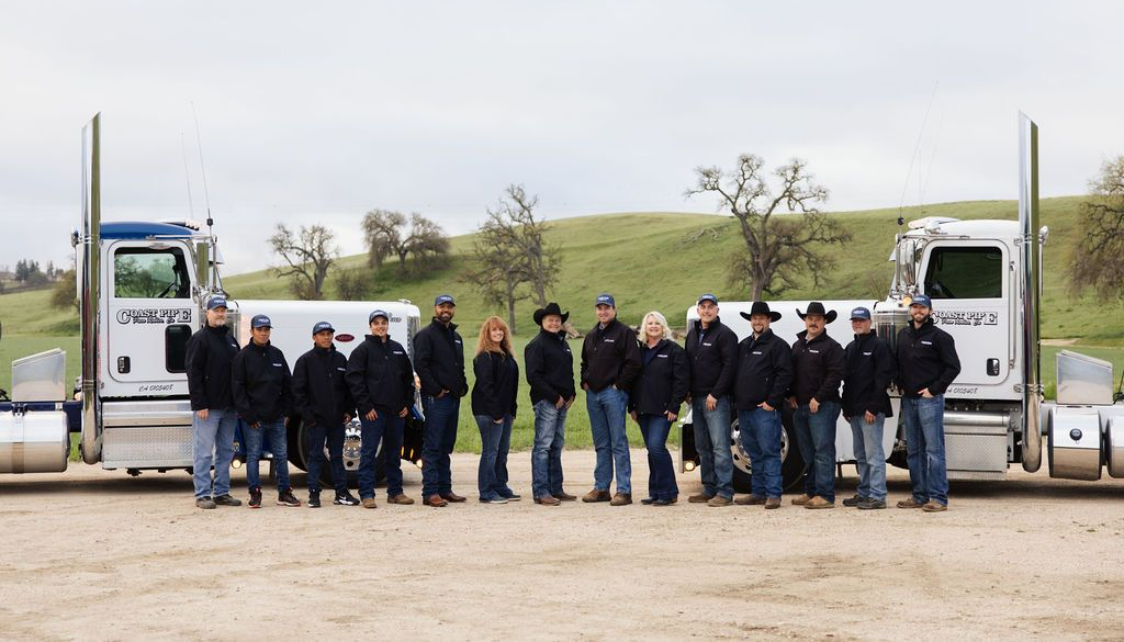 Group of workers standing between two white trucks on a gravel lot under an overcast sky