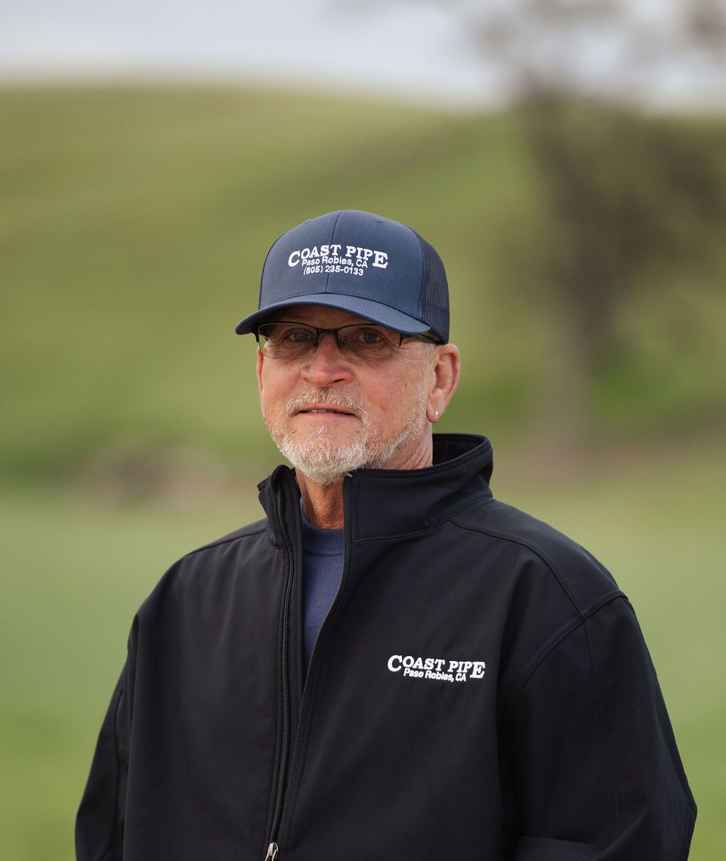 Person in a navy cap and black jacket standing outdoors on a blurred grassy hillside.