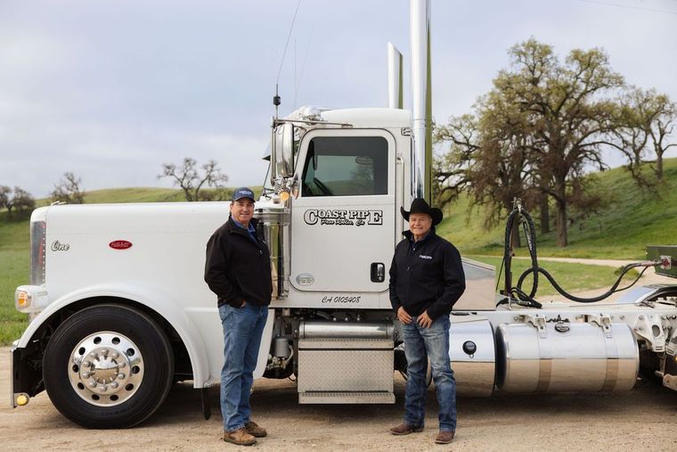 Two men standing by a white semi-truck in a rural area
