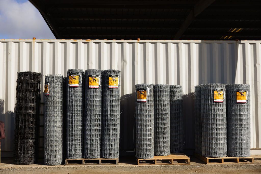 Rolled wire fence mesh stacked on wooden pallets outside a warehouse