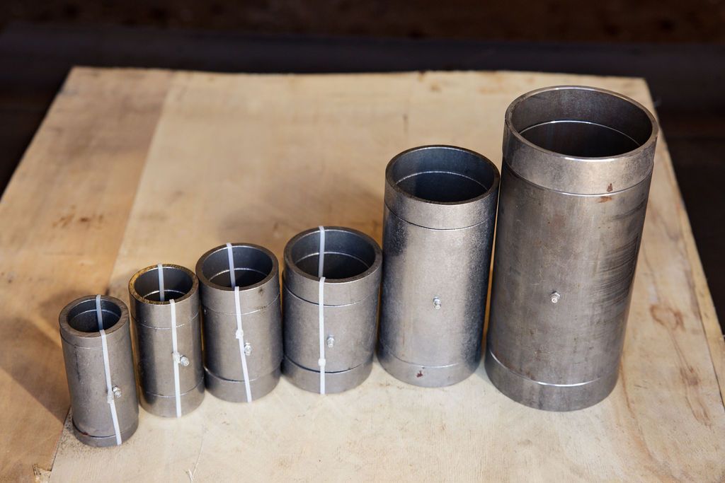 Five metal pipe sections of increasing size lined up on a wooden table.