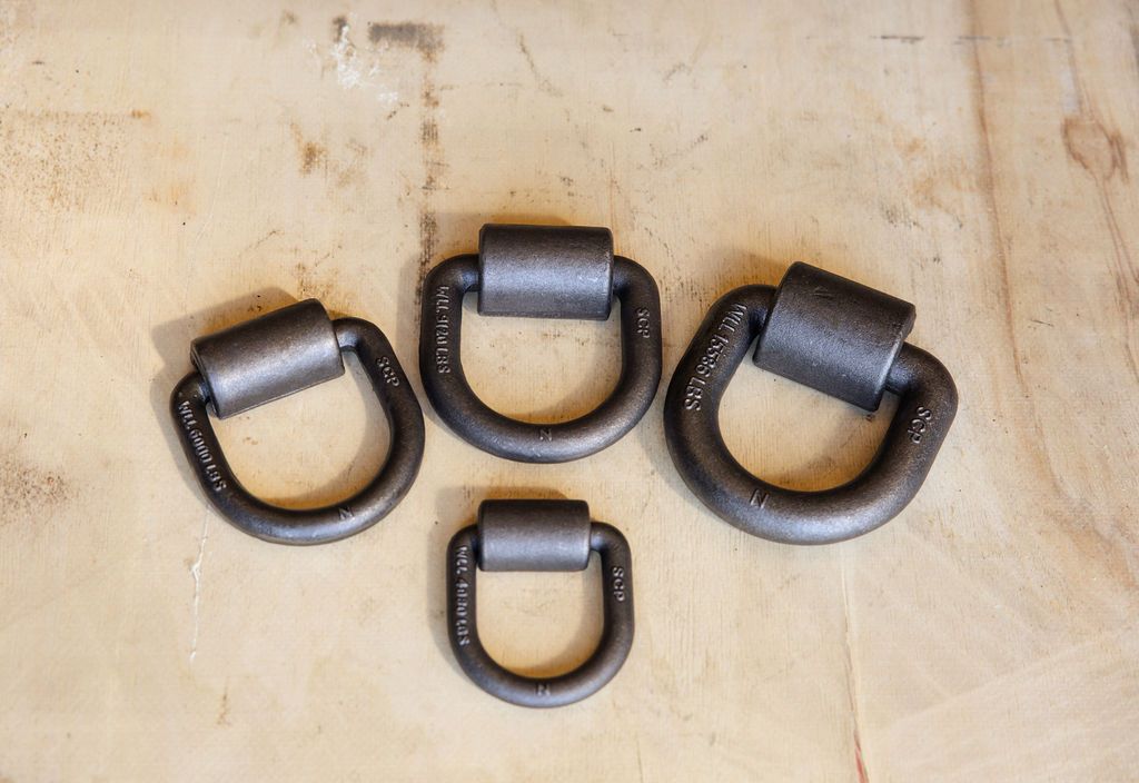 Four black metal D-rings with cylinders, arranged on a light wooden surface.