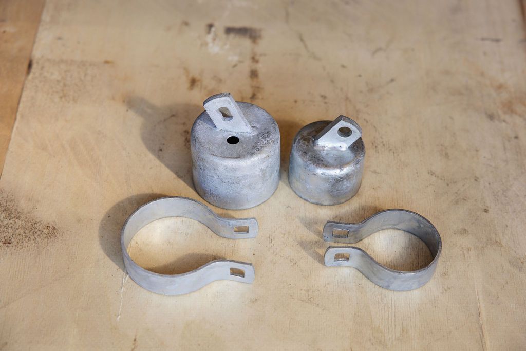 Four metal pipe clamps and two small fittings arranged on a wooden surface