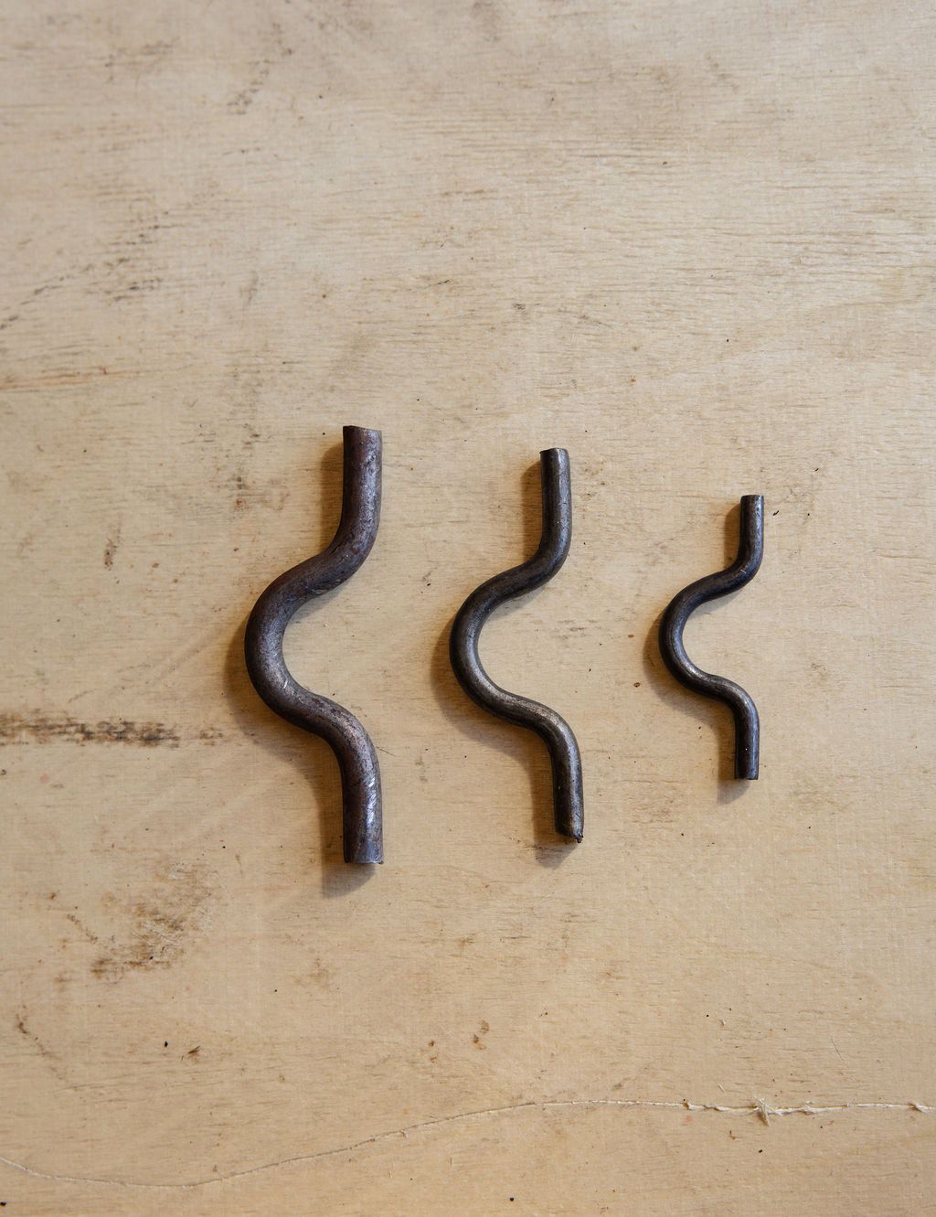 Three black wavy metal hooks lined up on a light wooden surface.