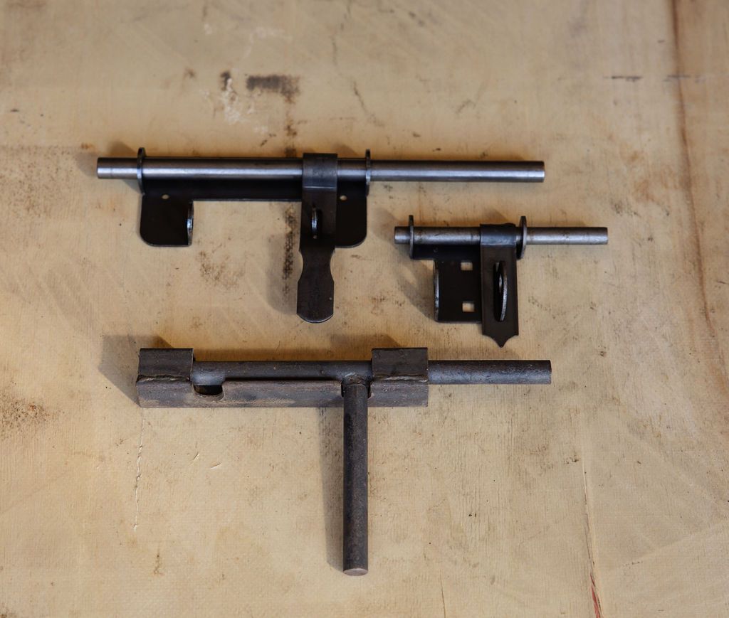 Three black metal clamps or brackets arranged on a light wooden surface.