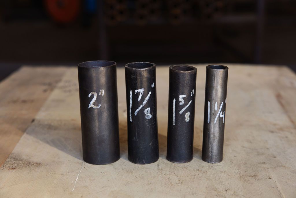 Four black metal cylinders of different diameters lined up on a wooden surface, labeled with white chalk numbers.