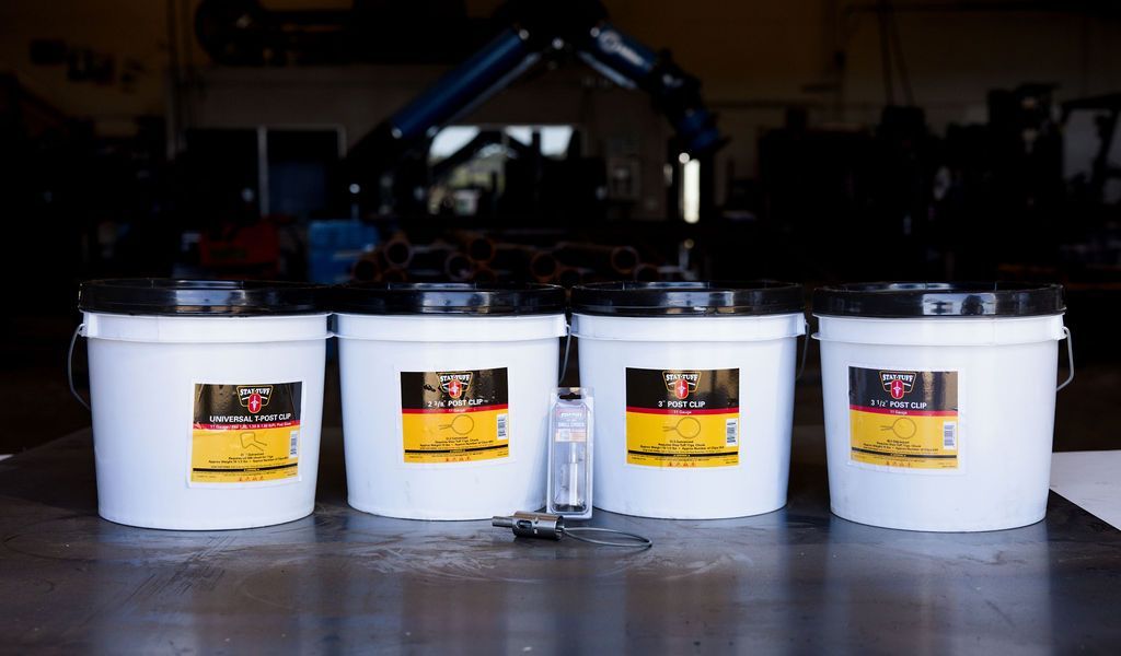 Four white plastic buckets with yellow labels lined up on a warehouse floor.