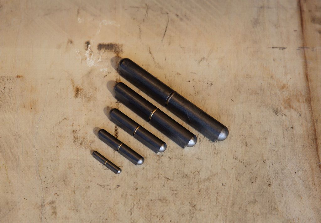 Five black metal drill bits arranged from largest to smallest on a worn wooden surface