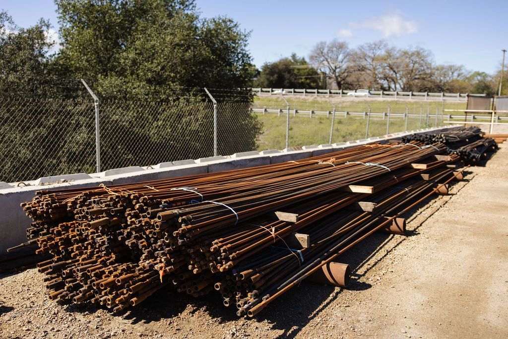 Stacks of steel rebar beside a chain-link fence at an outdoor construction site