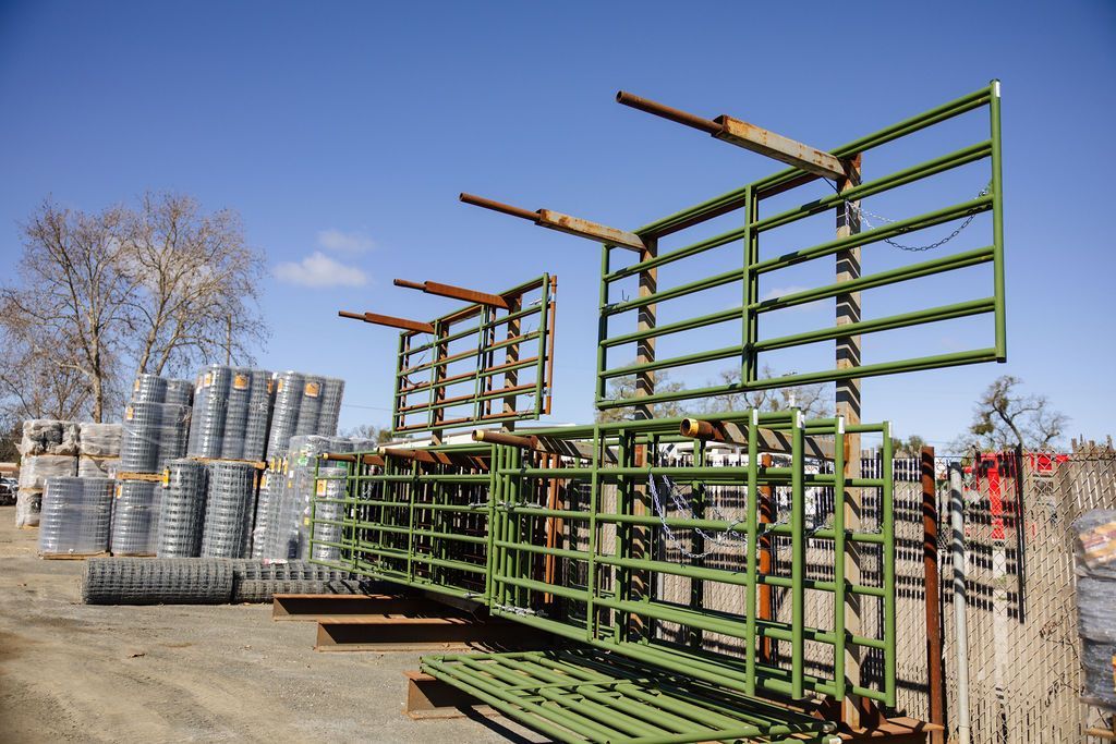 Green metal racks stacked in an outdoor yard beside piles of coiled wire under a clear sky