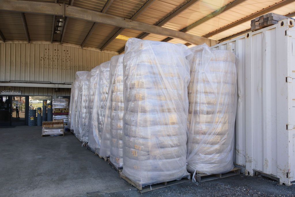Large wrapped bales stacked inside a warehouse beside a white shipping container.