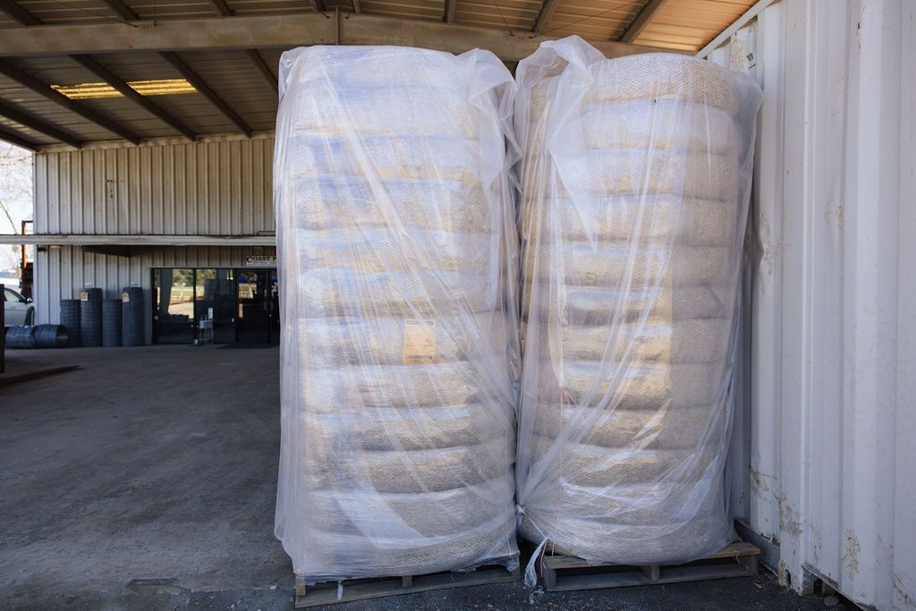 Two large white wrapped wattles stacked in a warehouse beside a corrugated metal wall