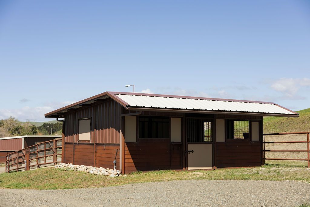 Small brown ranch-style building with a white roof and fenced yard under a clear sky