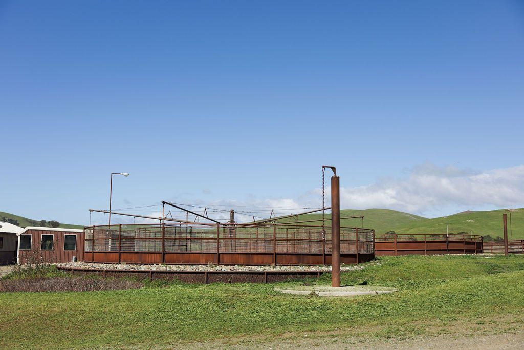 Rusty railcars on a track beside grassy hills under a blue sky