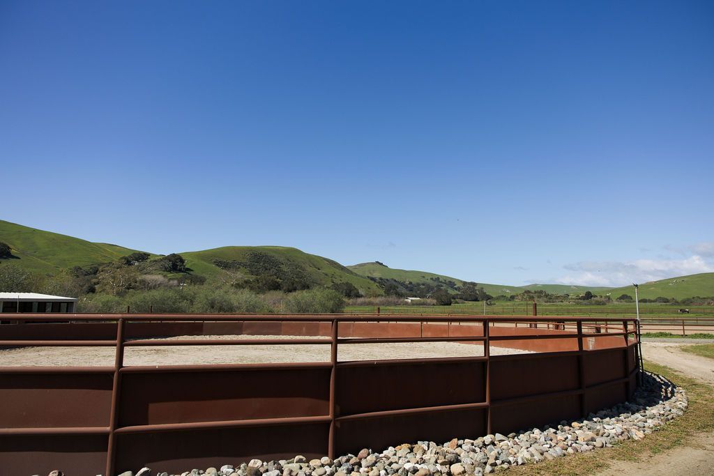 Rusty metal barrier beside a gravel path, with green hills under a clear blue sky.