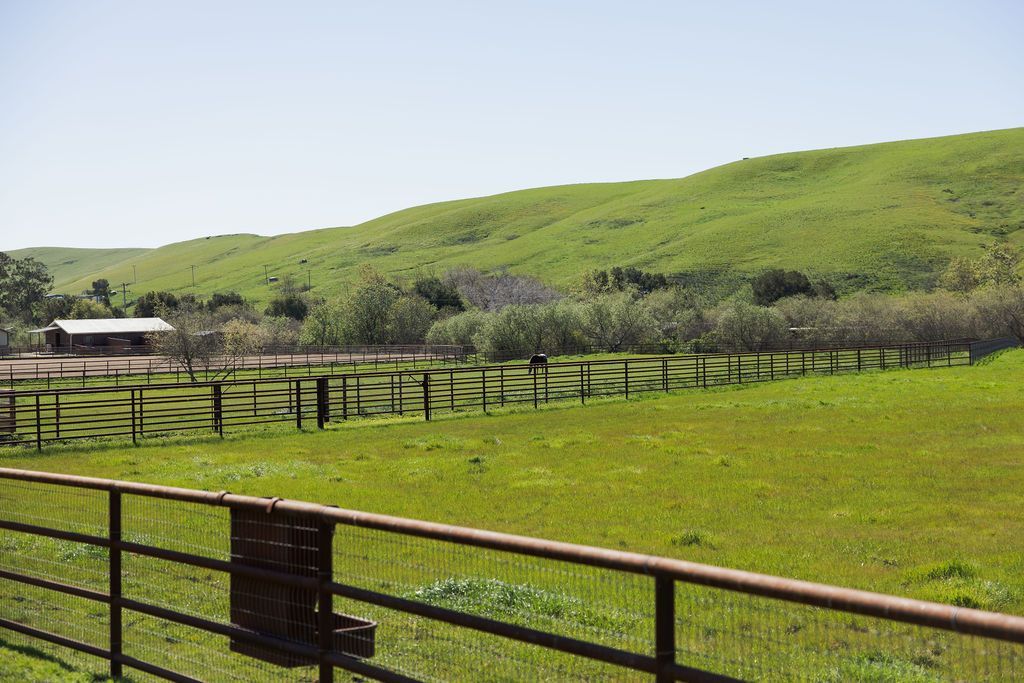 Green hillside pasture with wooden fences and a small barn under a clear sky