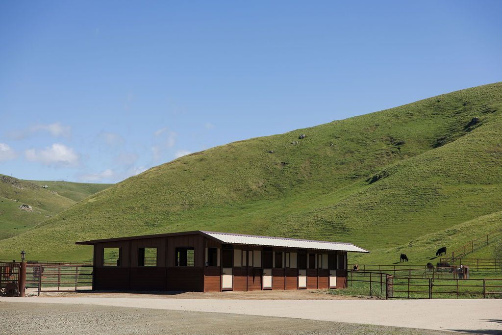 Small wooden building beside a fenced area in a grassy hillside landscape under a clear blue sky