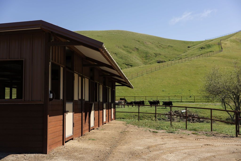 Rural building beside a fenced green hillside under a clear blue sky