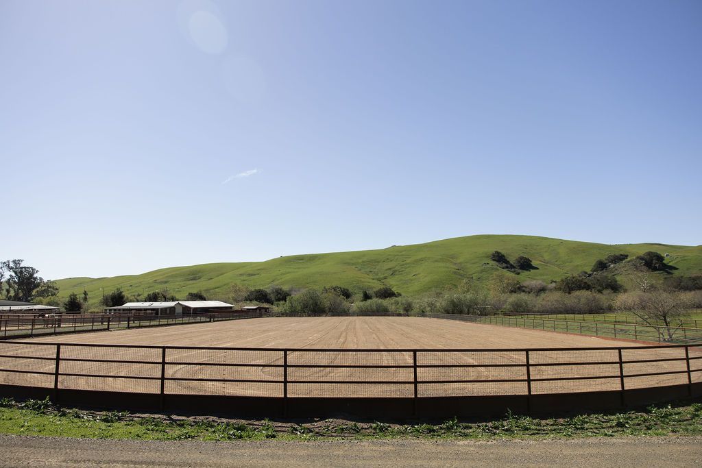 Fenced dirt arena with hills and a clear blue sky in the background