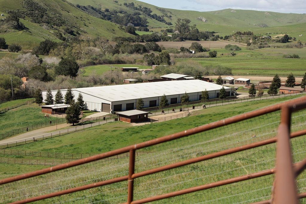 White event tent in a green valley with rolling hills and red fence in the foreground