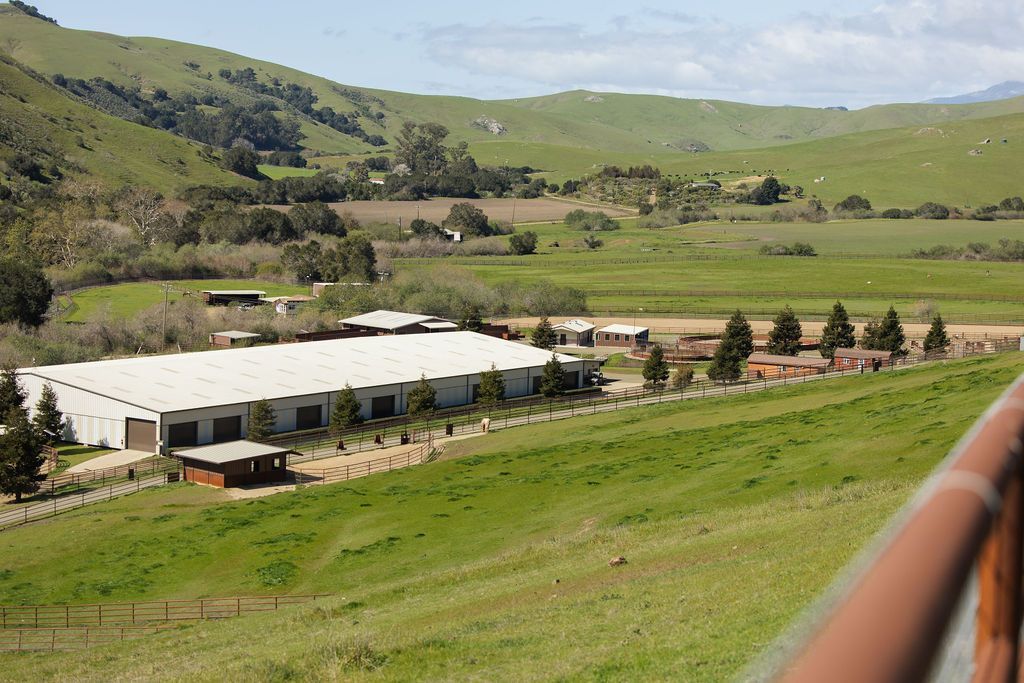 White warehouse in green countryside with rolling hills and a railing in the foreground