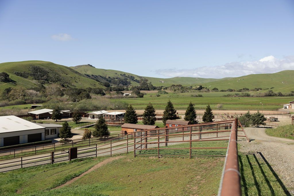 Rural valley with green hills, fenced fields, and farm buildings under a clear blue sky