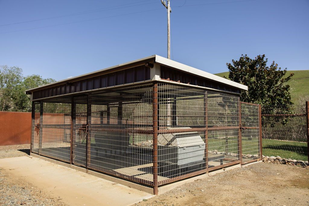 Small fenced enclosure with a metal-roofed shelter and parked vehicle on a dirt lot, under a clear sky