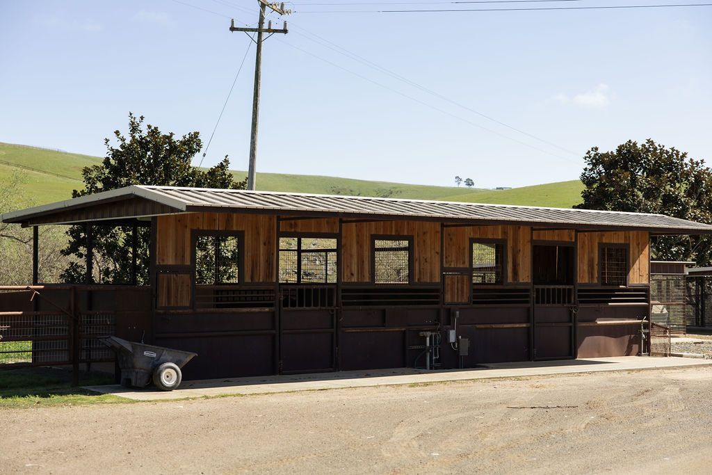 Rustic wooden building with a corrugated roof along a dirt road in a rural landscape