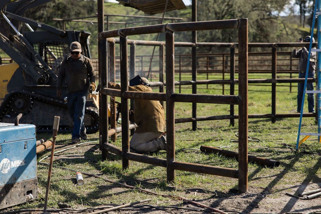 Person near a tractor and wooden fence panels in a grassy outdoor work area