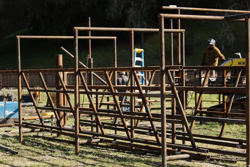 Outdoor obstacle course made of metal frames and wooden platforms, with two people on a sunny field