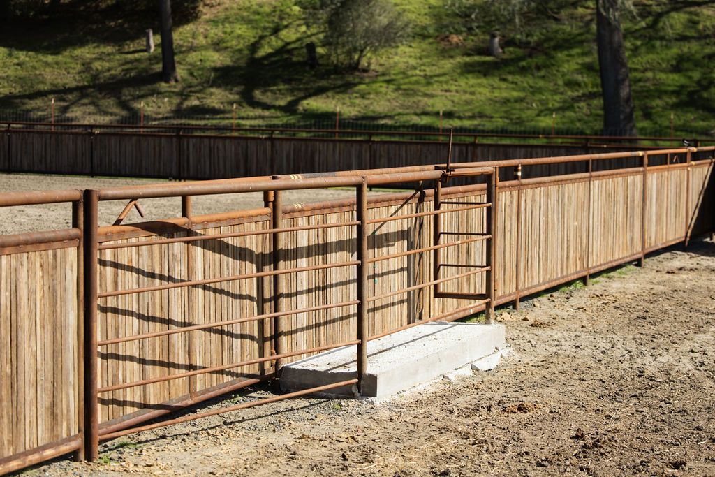 Rust-colored metal gate and tan fence along a gravel path in a grassy outdoor area